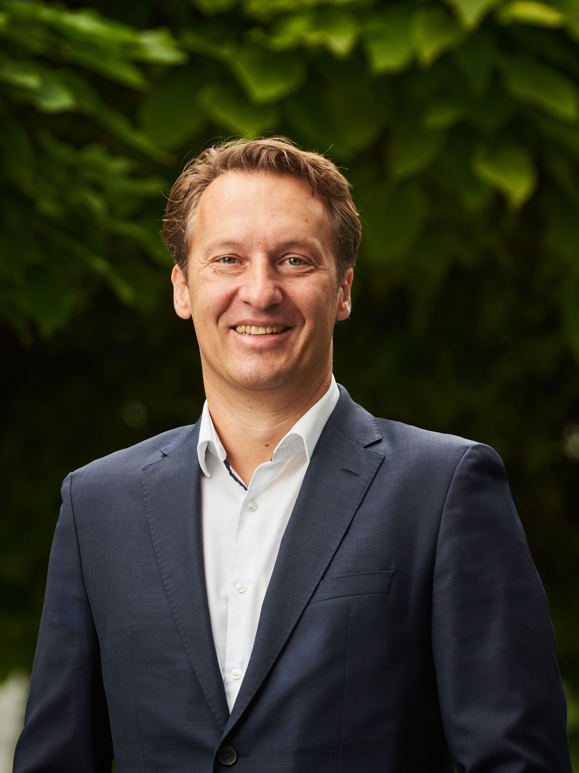 Venku stojí usměvavý muž v obleku.